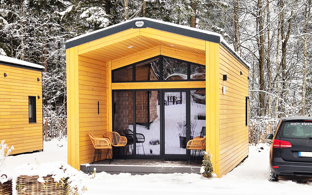 Romatisch verschneeites Chalet in der Aussenansicht in der Skiregion Sudelfeld und Spitzingsee. Im Tiefschnee parkt nebem dem Chalet ein Auto auf dem privaten Parkplatz.