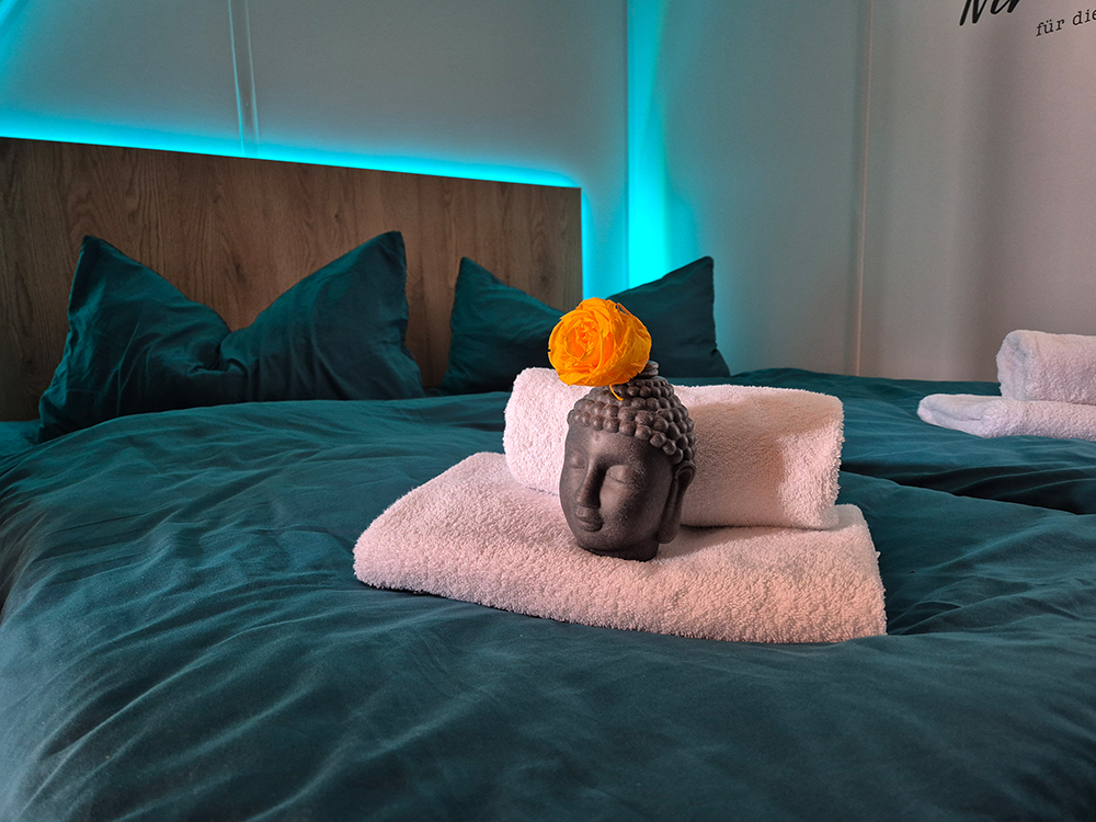 ein Doppelbett in der Morgensonne vorbereitet für Gäste mit dekorativen Handtüchern und Buddha für erholsame Nächte im Chalet mit stimmungsvoller indirekter Hintergrundbeleuchtung