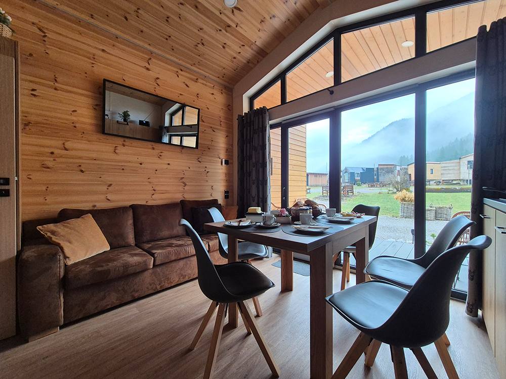 Reich gedeckter Frühstückstisch mit frischen Backwaren vom regionalem Bäcker im Josefstal, dampfenden frisch aufgebrühtem Kaffee in einem modernen Alpenchalet mit Panorama-Aussicht auf die Berge Aiplspitz und Jaegerkamp durch große Süd-Fensterfront in der Urlaubsregion Tegernsee Schliersee.